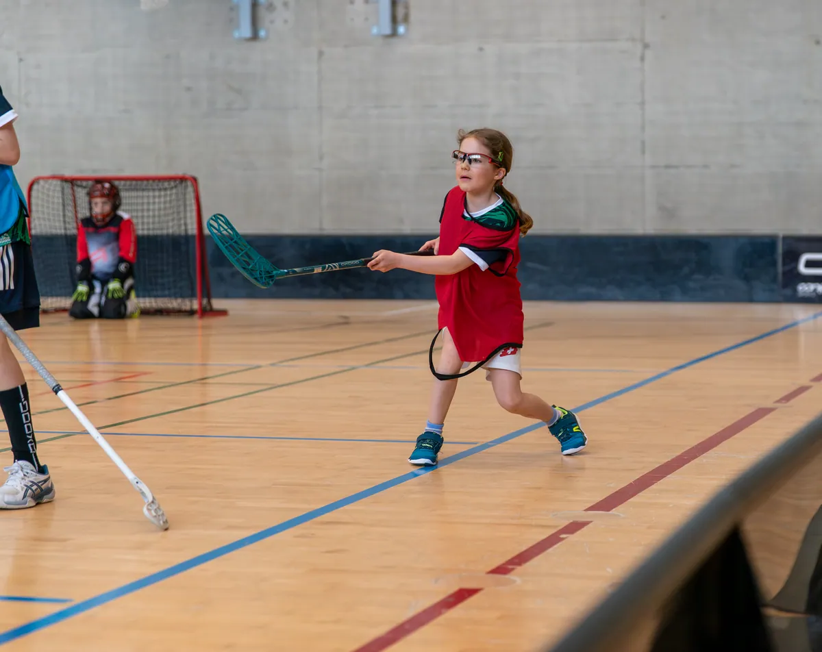 Junge Unihockeyspielerin mit Schutzbrille beim ersten Pass